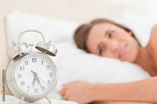 Woman in bed with her alarm clock beside her showing the time
