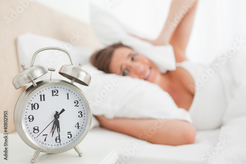 Woman covering her ears with a pillow as her alarm rings
