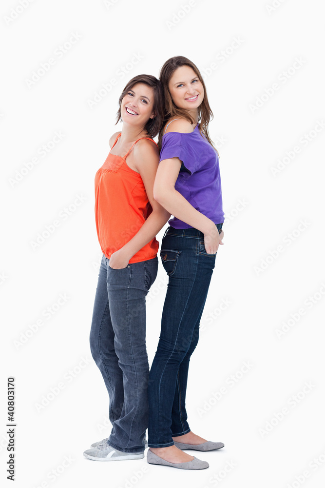 Relaxed teenagers standing back to back with their hands in thei Relaxed teenagers standing back to back with their hands in thei