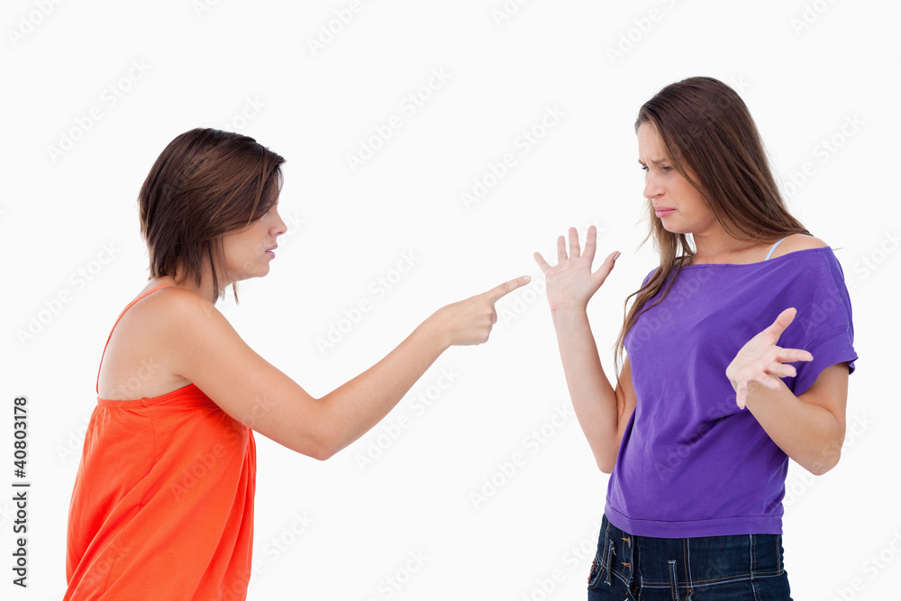 Teenage girl accusing her friend while pointing finger at her Teenage girl accusing her friend while pointing finger at her