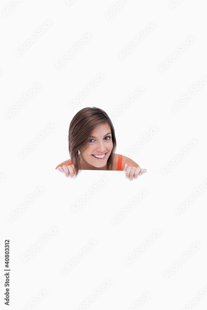 Smiling teenage girl standing behind a blank poster Smiling teenage girl standing behind a blank poster