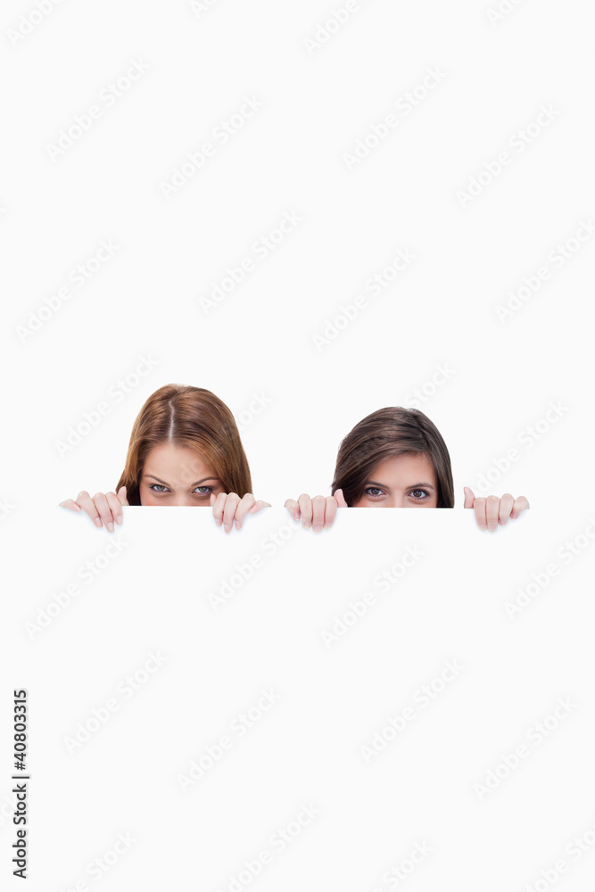 Two friends secretly hiding behind a blank poster Two friends secretly hiding behind a blank poster