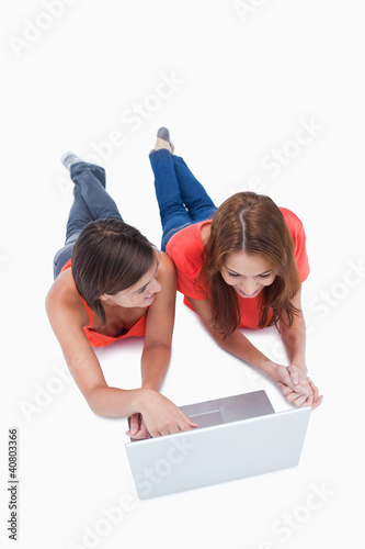 Teenage girl using a laptop while looking at her friend and lyin photo