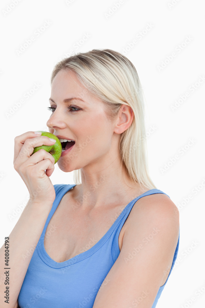 Blonde woman looking to the side while eating a green apple Blonde woman looking to the side while eating a green apple