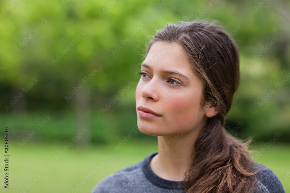Thoughtful young woman standing in a park while looking towards Thoughtful young woman standing in a park while looking towards