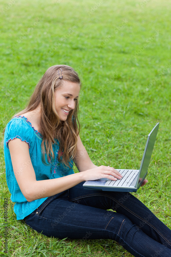 Young smiling girl typing on her laptop while sitting down on th Young smiling girl typing on her laptop while sitting down on th