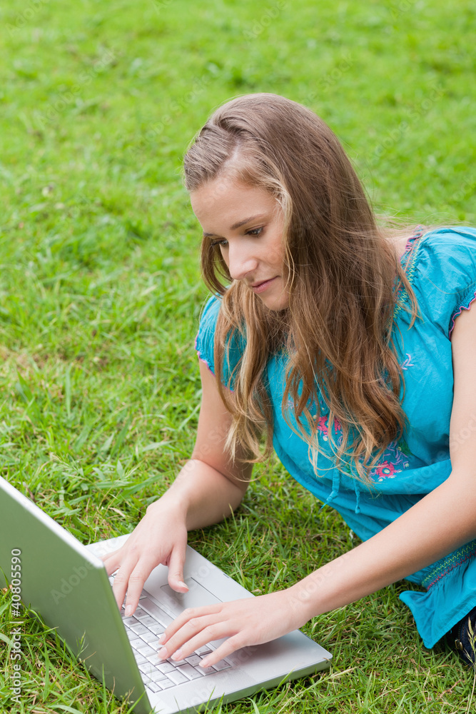 Young serious girl lying on the grass while using her laptop Young serious girl lying on the grass while using her laptop