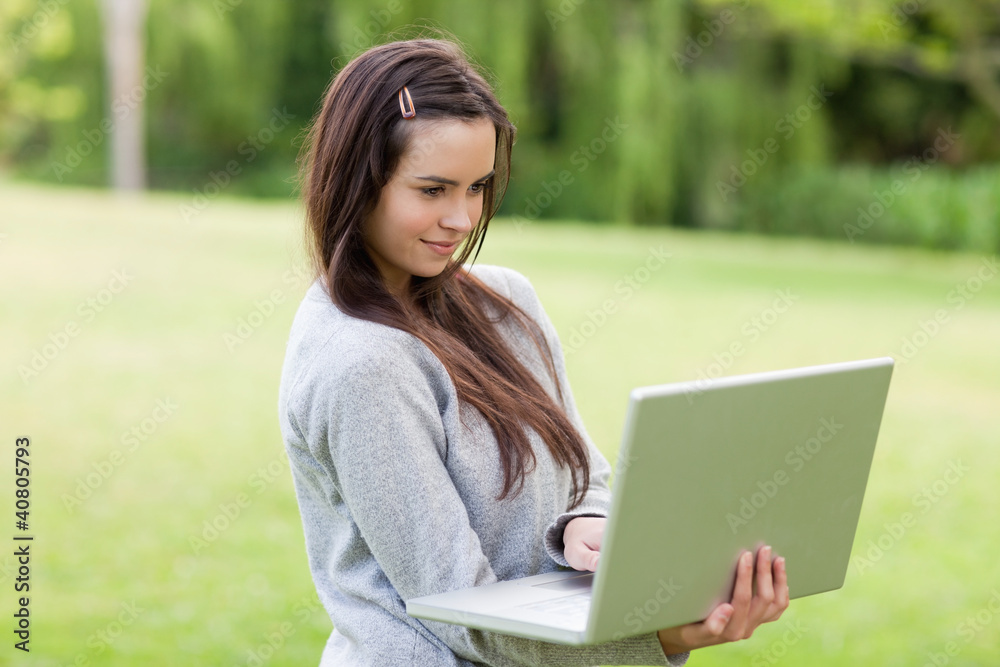 Serious young woman standing upright in a park while holding her Serious young woman standing upright in a park while holding her