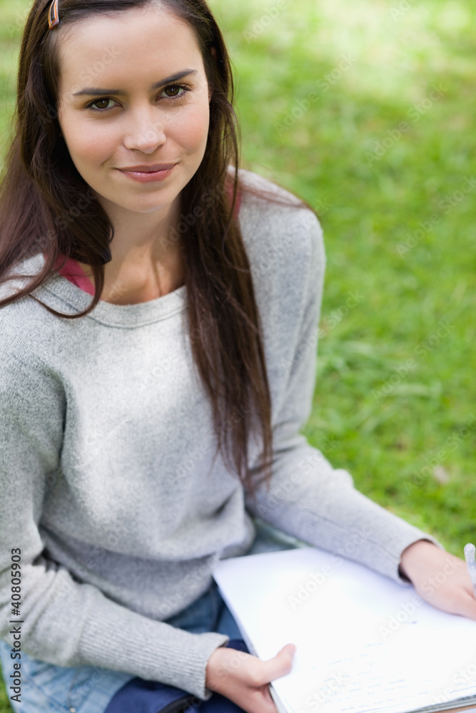 Young calm girl sitting in a park while holding school books Young calm girl sitting in a park while holding school books
