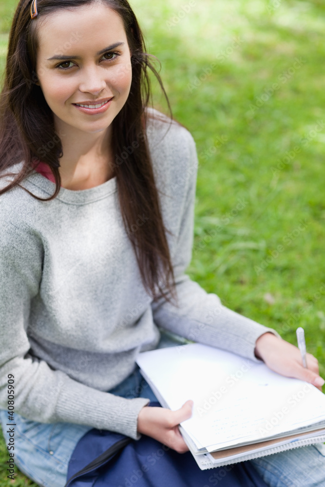 Obraz premium Smiling young girl sitting in a park while looking at the camera