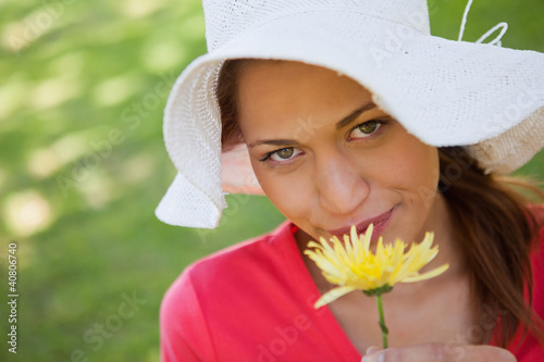 Woman wearing a white hat while smelling a yellow flower