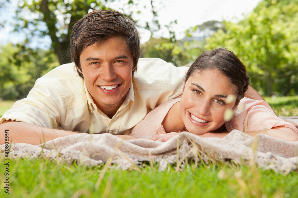 Two friends smiling and looking ahead while lying on a blanket Two friends smiling and looking ahead while lying on a blanket