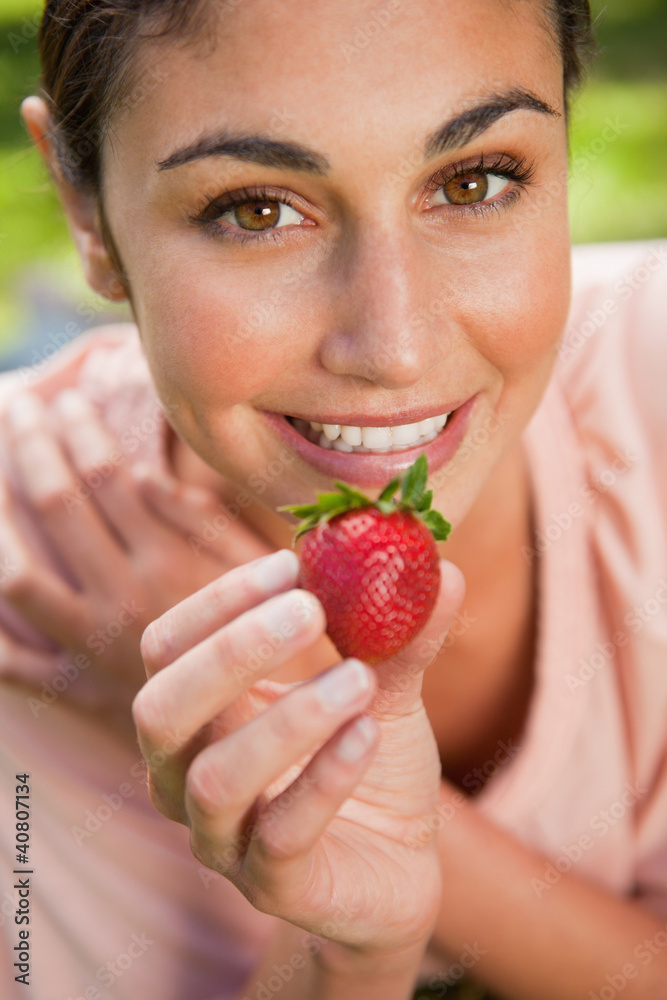 Woman offering a strawberry while lying in grass Woman offering a strawberry while lying in grass