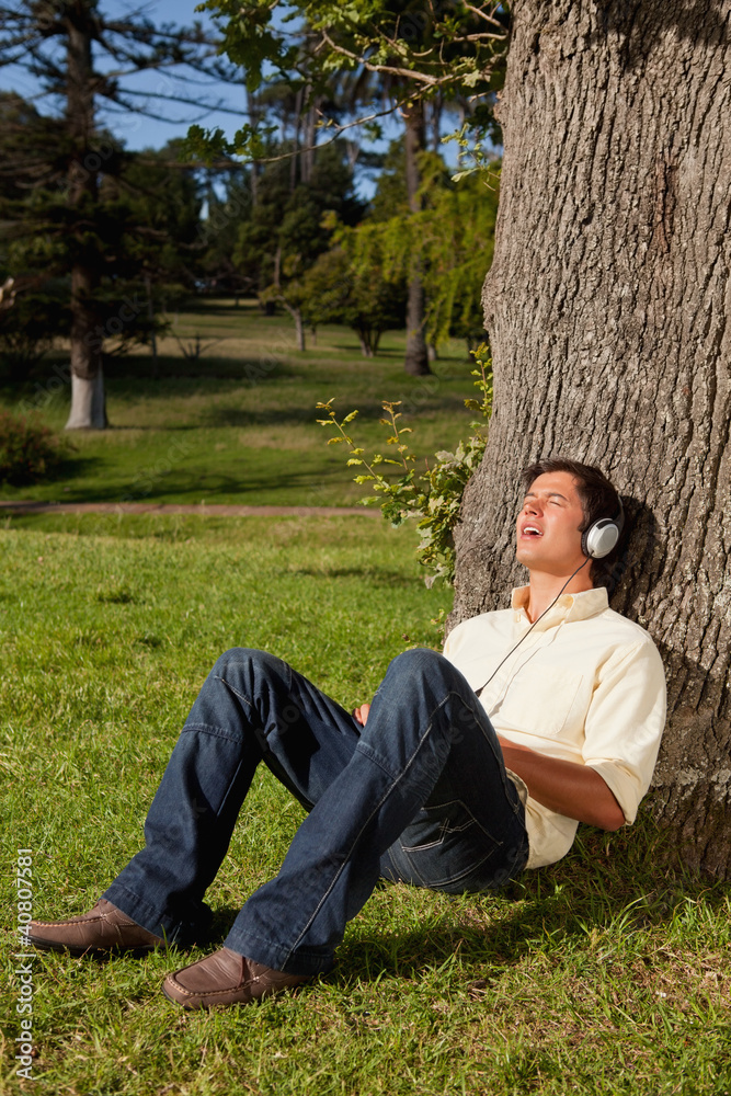 Man using headphones to sing along to music while resting a tree Man using headphones to sing along to music while resting a tree