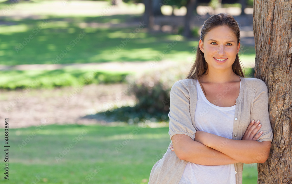 Smiling woman with her arms folded and leaning against a tree Smiling woman with her arms folded and leaning against a tree