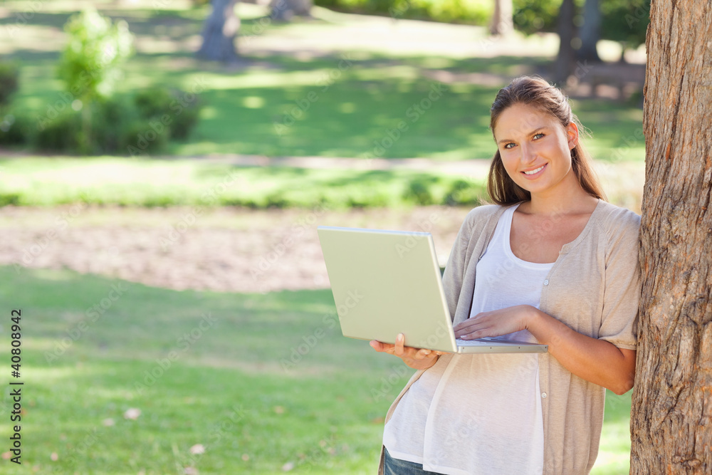 Smiling woman with a notebook leaning against a tree Smiling woman with a notebook leaning against a tree