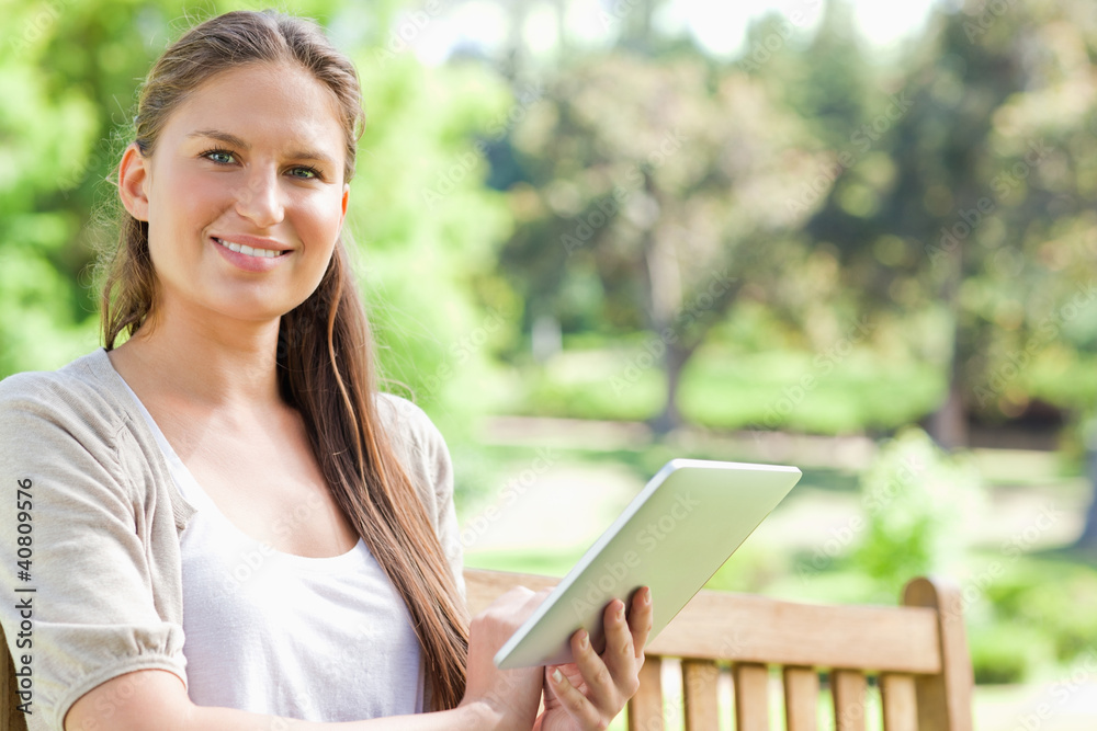 Fototapeta premium Smiling woman with a tablet on a park bench