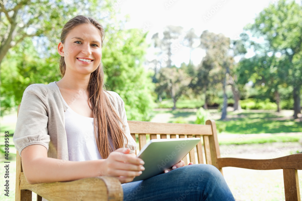 Obraz premium Smiling woman on a bench in the park with her tablet computer