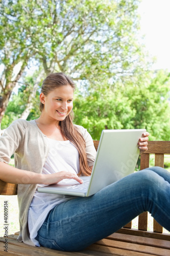 Smiling woman with her laptop sitting on a bench