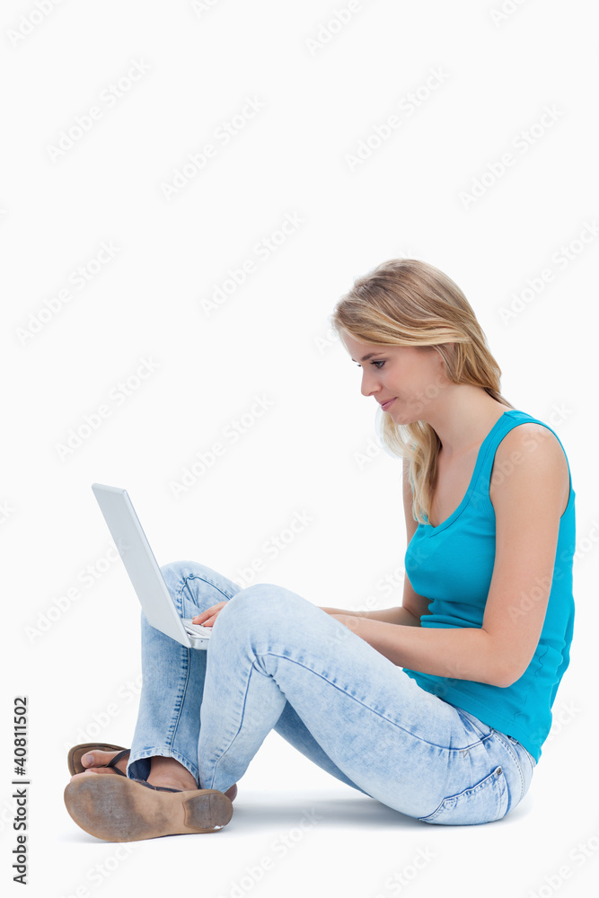 Naklejka premium A side view of a woman sitting on the ground typing on a laptop