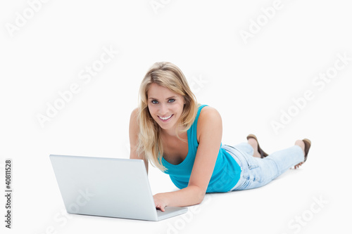 A smiling woman is lying on the floor with a laptop in front of © WavebreakmediaMicro