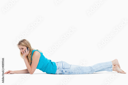 A happy woman lying on the floor is talking on her mobile phone