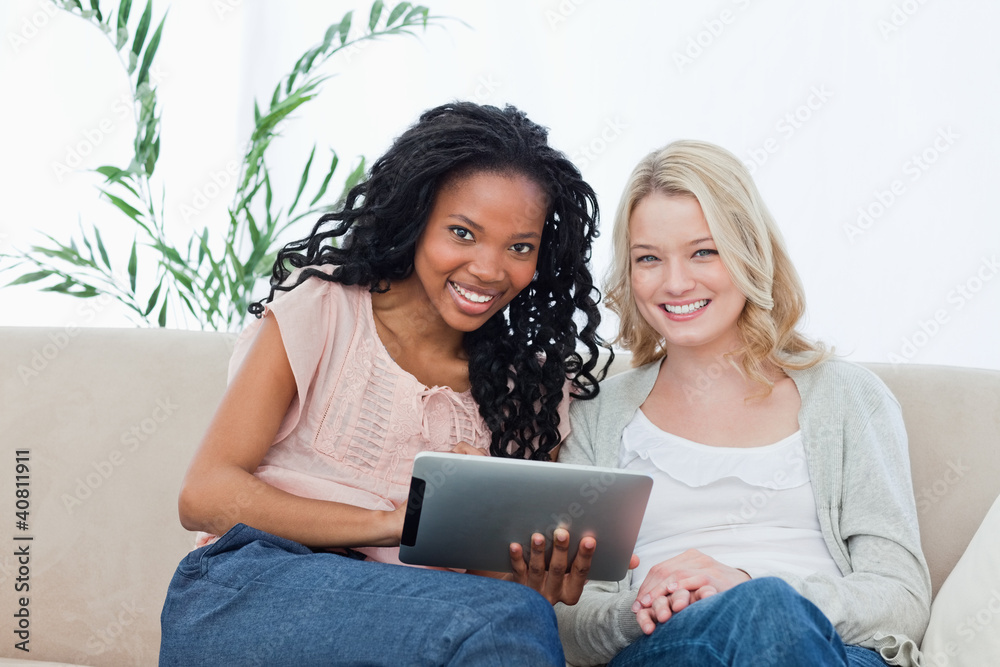 Two women smiling at the camera with a tablet computer in front Two women smiling at the camera with a tablet computer in front