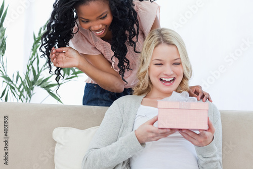 A surprised woman is holding a present with her friend standing