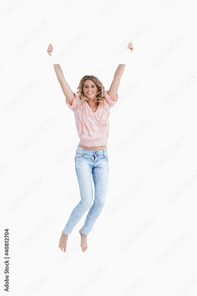 Smiling young woman jumping while holding a blank poster Smiling young woman jumping while holding a blank poster