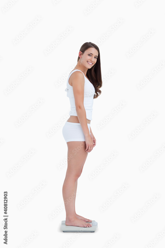 Smiling woman standing on weighing scales while looking at the c Smiling woman standing on weighing scales while looking at the c