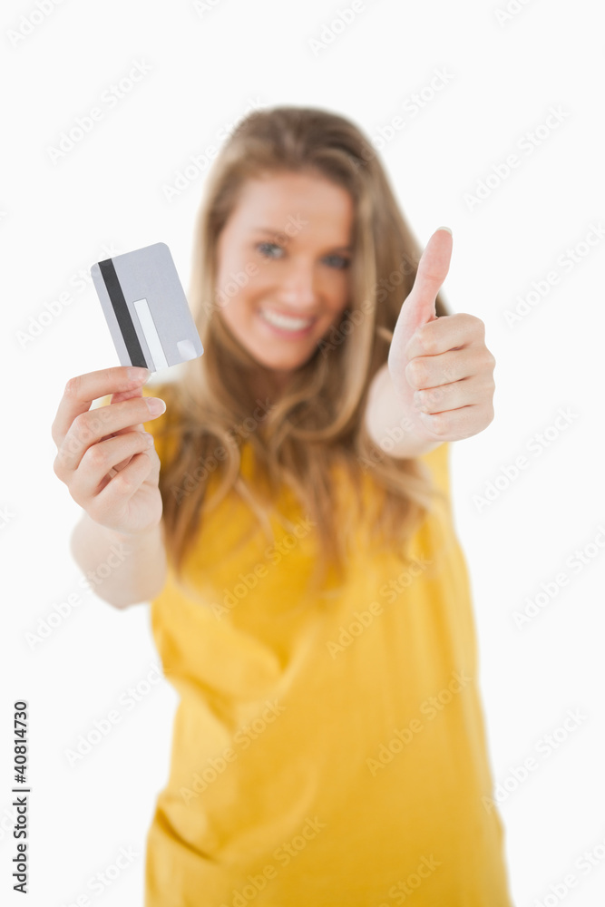 Portrait of a blonde student tending a credit card with the thum Portrait of a blonde student tending a credit card with the thum