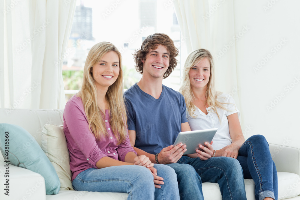 Three young adults look at the camera as they hold a tablet in t