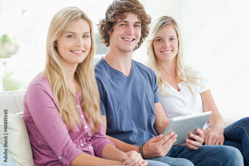 three siblings sit together as they use a tablet and look at the three siblings sit together as they use a tablet and look at the