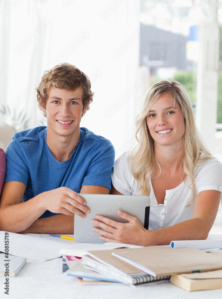 A smiling couple hold a tablet as they both look into the camera A smiling couple hold a tablet as they both look into the camera