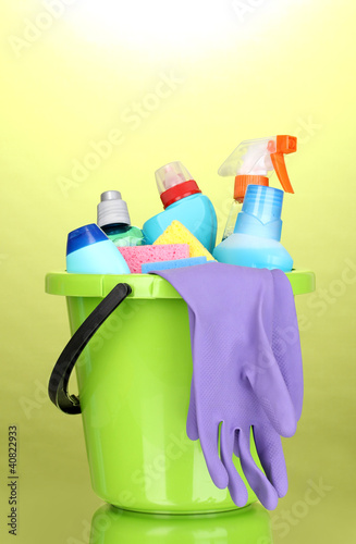 Bucket with cleaning items on green background