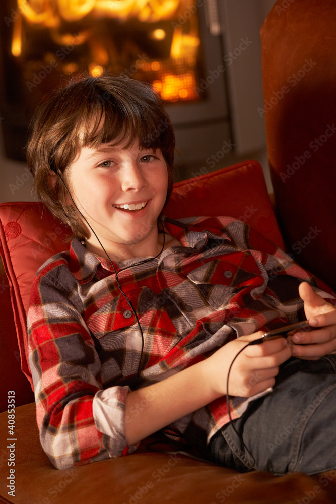 Young Boy Relaxing With MP3 Player By Cosy Log Fire