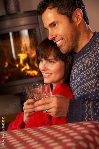 Middle Aged Couple Sitting On Sofa Watching TV By Cosy Log Fire