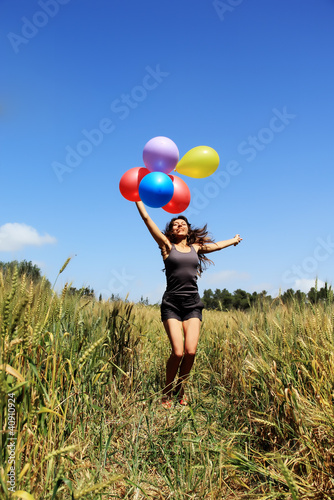 Young woman holding colorful balloons and flying over a meadow