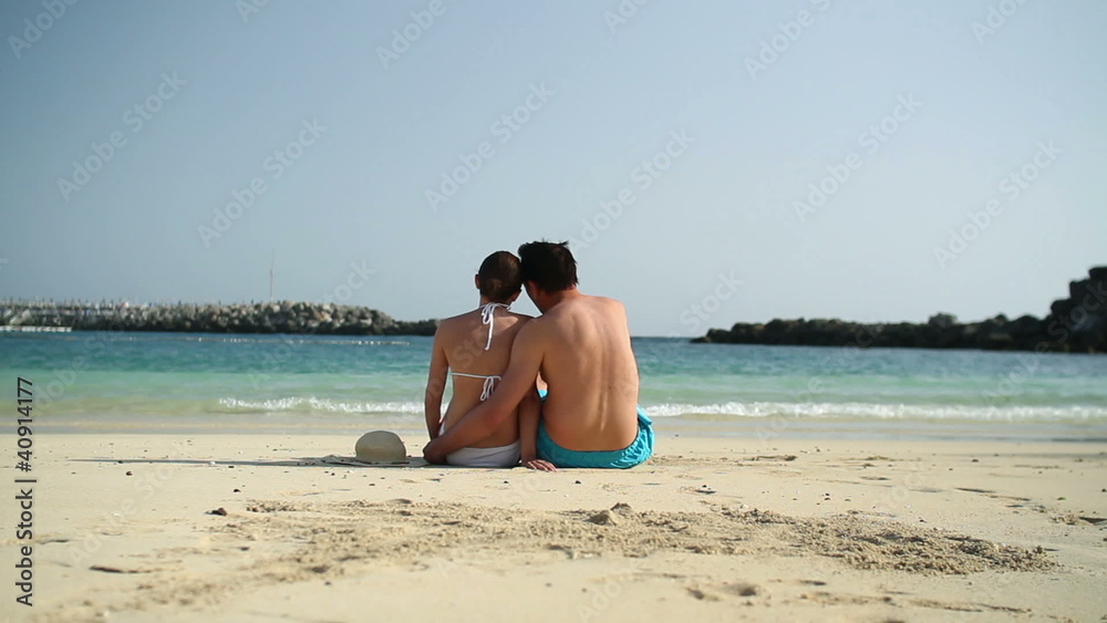 Couple sitting close together on the beach, rear view Couple sitting close together on the beach, rear view