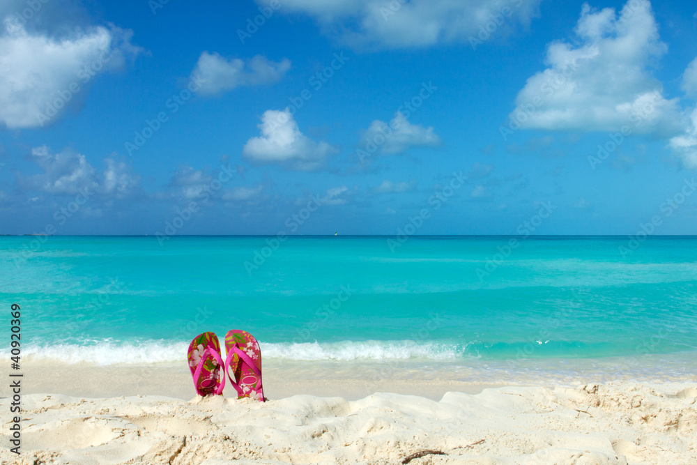 Fototapeta premium Pair of colored sandals on a white sand beach