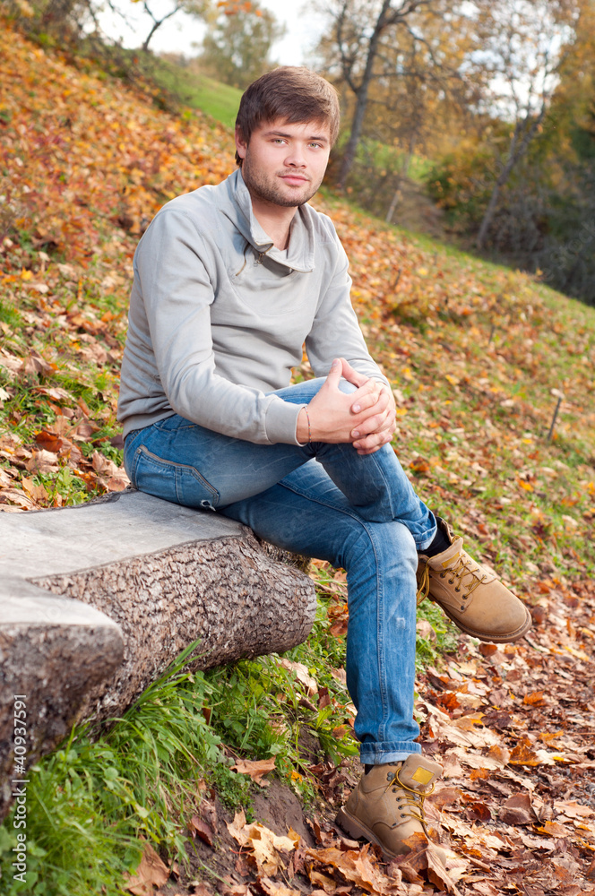 Outdoors portrait of happy young man sitting in autumn park Outdoors portrait of happy young man sitting in autumn park