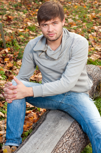 Outdoors portrait of happy young man sitting in autumn park