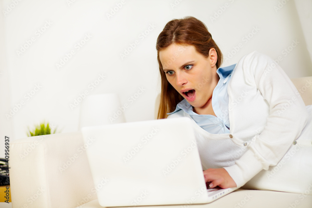 Surprised woman lying on sofa with a laptop Surprised woman lying on sofa with a laptop