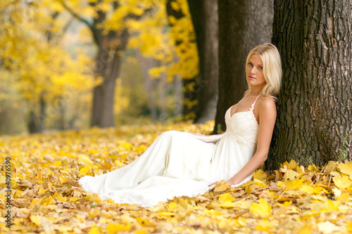 Beautiful young bride sitting in autumnal park