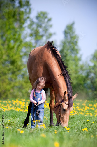 Child and big horse standing in the field at spring.