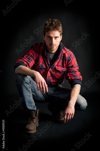 Portrait of young man crouched against black background.