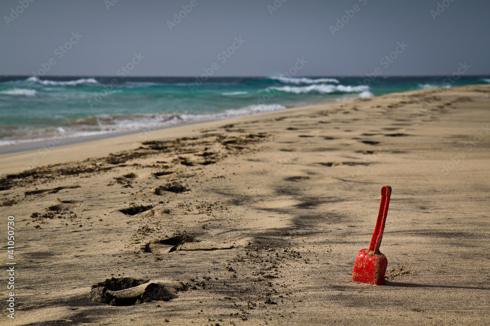 A single red shovel on a secluded sandy beach.