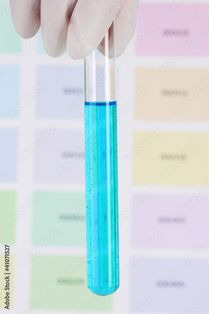 Tube with blue liquid in hand on color samples background Tube with blue liquid in hand on color samples background