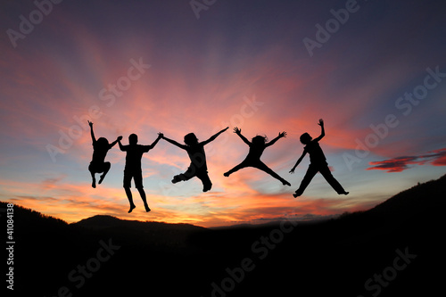 silhouette of teens jumping in front of mountain range