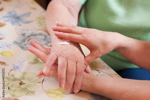Altenpflegerin cremt Seniorin die Hand photo